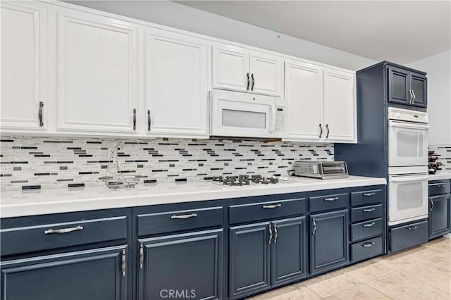 kitchen with white appliances, backsplash, white cabinets, and light tile patterned floors