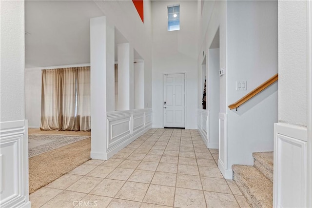 entryway with light tile patterned floors, stairway, a decorative wall, wainscoting, and light carpet