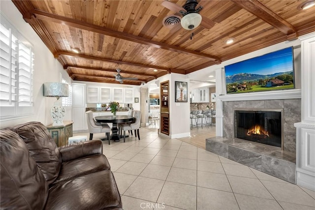 living room featuring wood ceiling, light tile patterned floors, a ceiling fan, beamed ceiling, and a premium fireplace