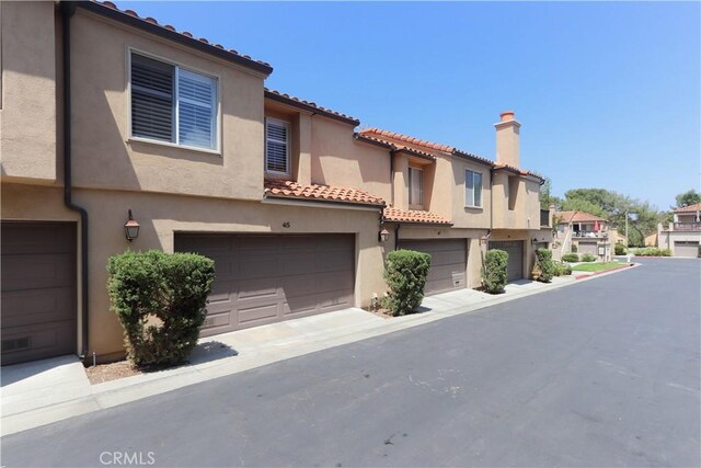 view of front of home with an attached garage, a chimney, a residential view, a tiled roof, and stucco siding