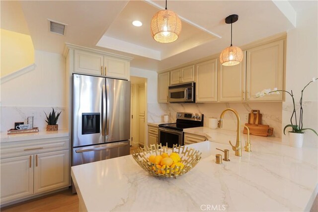 kitchen featuring stainless steel appliances, a tray ceiling, light stone counters, decorative light fixtures, and decorative backsplash