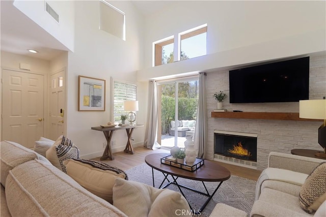 living area featuring wood finished floors, a stone fireplace, baseboards, and a towering ceiling