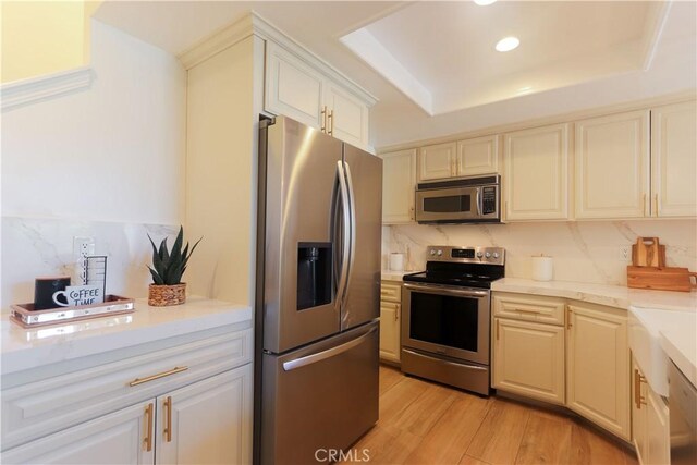 kitchen with stainless steel appliances, light wood-style floors, a raised ceiling, tasteful backsplash, and recessed lighting