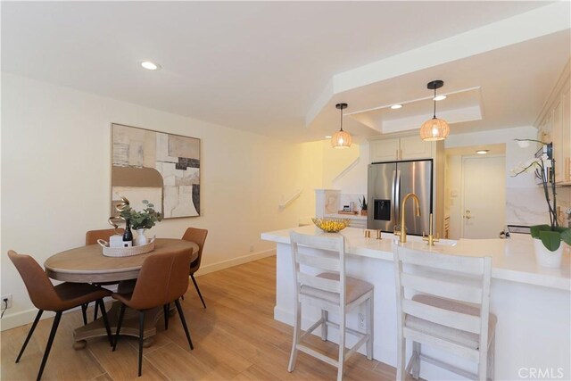 kitchen featuring stainless steel refrigerator with ice dispenser, a raised ceiling, a peninsula, light countertops, and light wood-type flooring