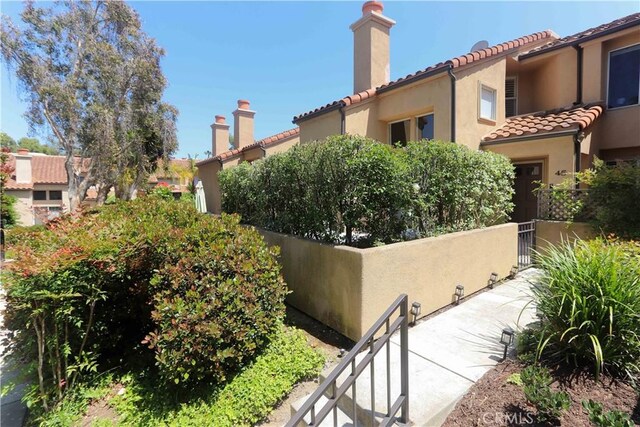 view of side of property featuring a tiled roof, a chimney, fence, and stucco siding