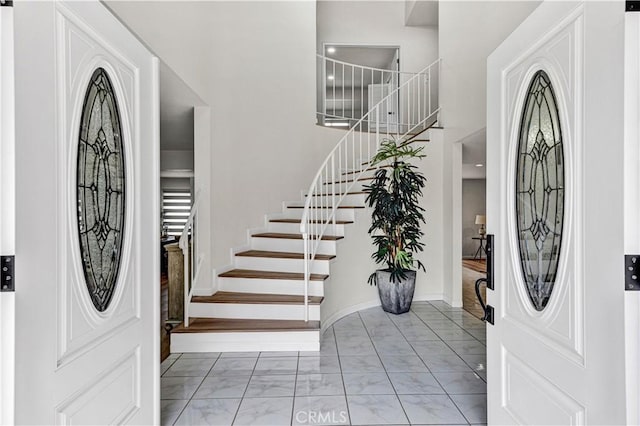 foyer with light marble finish floors, stairway, and a high ceiling