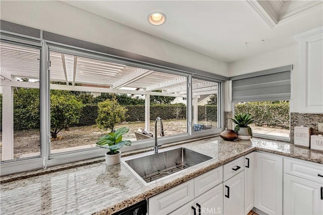 kitchen featuring a sink, white cabinetry, light stone counters, and backsplash