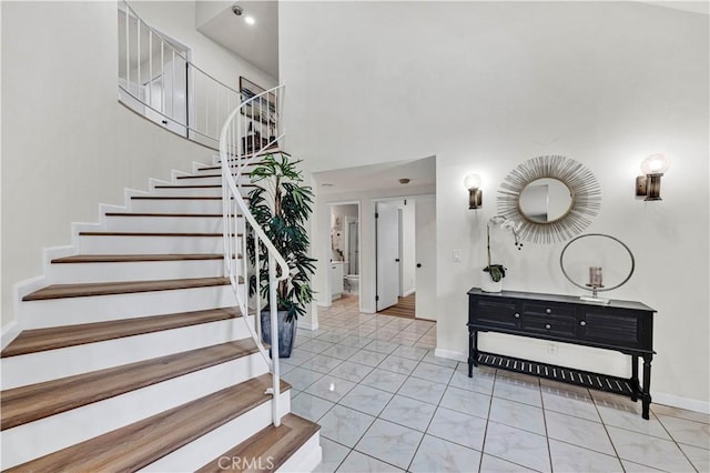 tiled foyer featuring baseboards, stairs, and a high ceiling