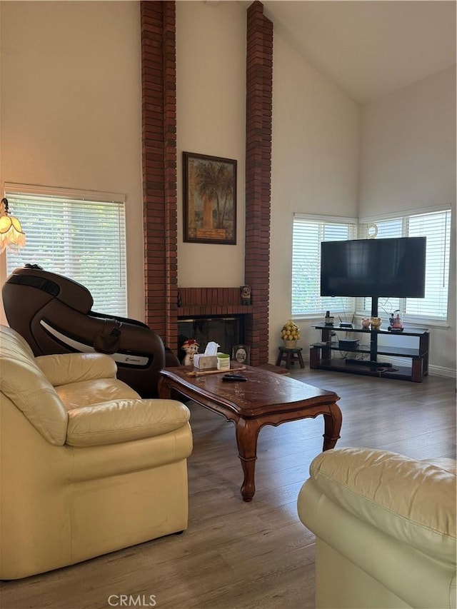 living room with high vaulted ceiling, wood finished floors, a brick fireplace, and healthy amount of natural light