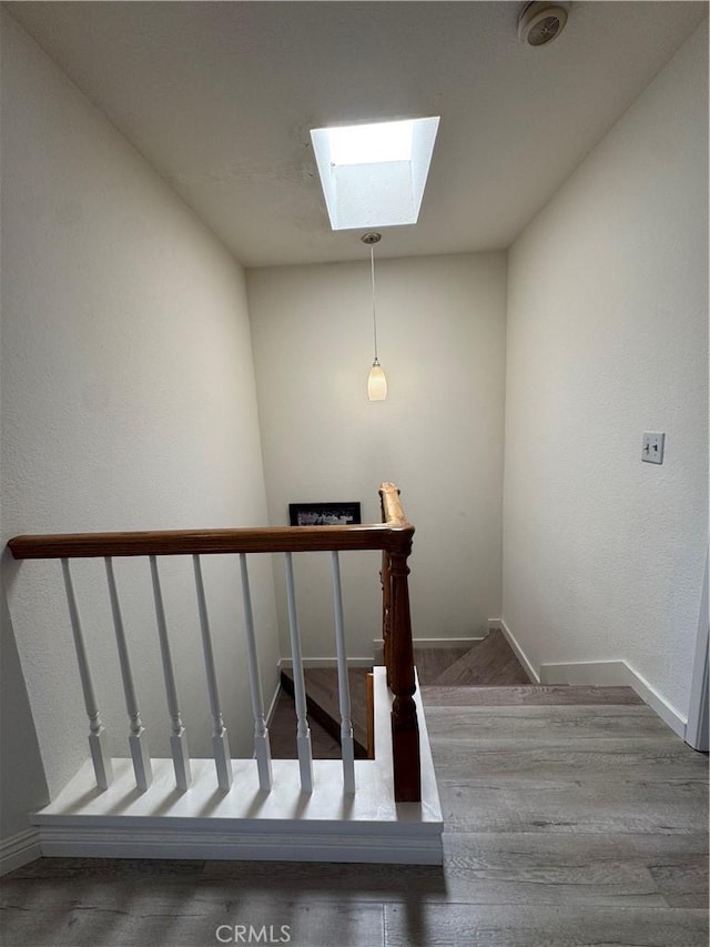 stairway featuring a skylight, wood finished floors, and baseboards