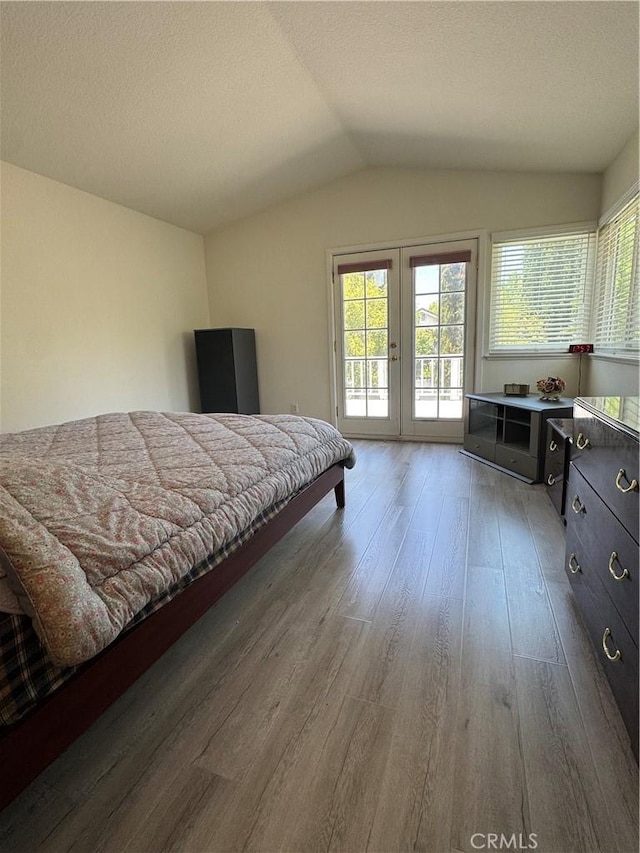 bedroom with access to exterior, wood finished floors, lofted ceiling, french doors, and a textured ceiling
