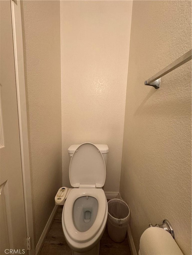 bathroom with toilet, baseboards, and a textured wall