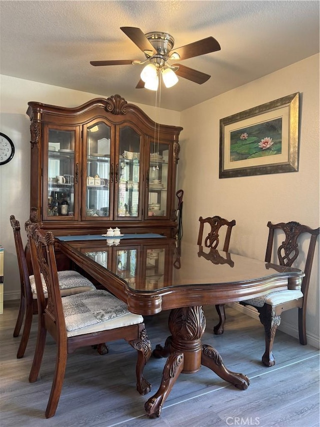dining area with wood finished floors, a ceiling fan, baseboards, and a textured ceiling