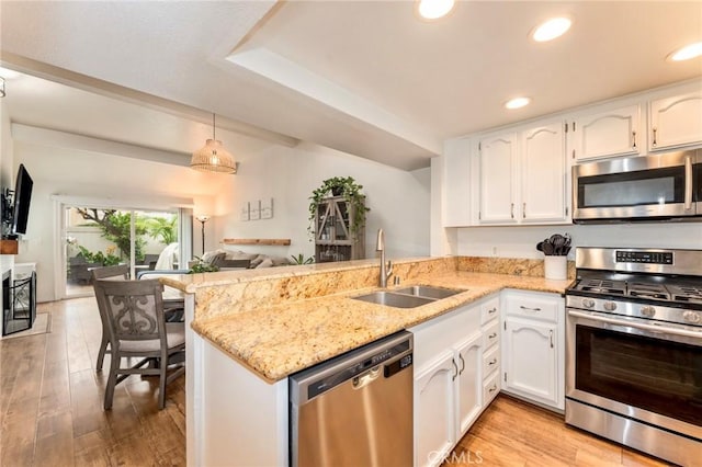kitchen featuring stainless steel appliances, a sink, white cabinets, a peninsula, and light wood-style flooring