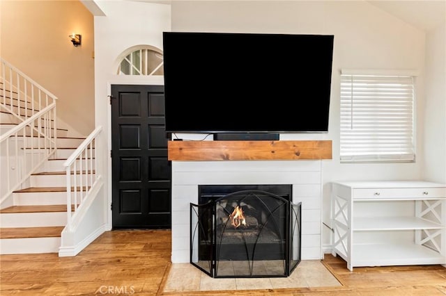 living area featuring light wood-style floors, stairway, and a fireplace with flush hearth