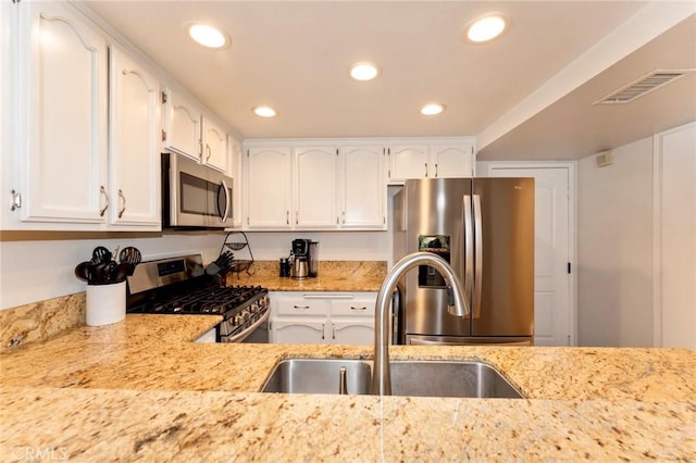 kitchen with appliances with stainless steel finishes, a sink, white cabinets, recessed lighting, and light stone countertops
