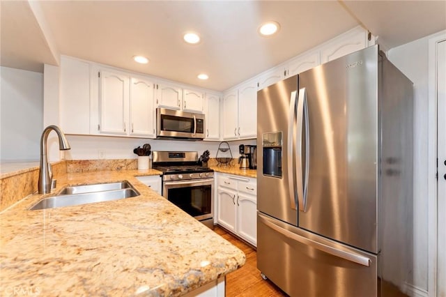 kitchen featuring stainless steel appliances, a sink, recessed lighting, white cabinetry, and light wood-style floors