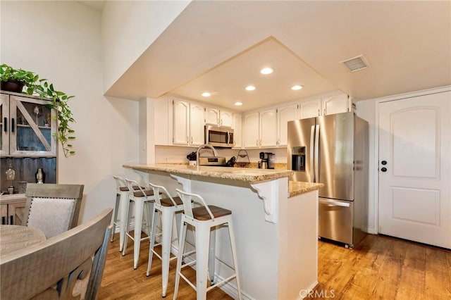 kitchen with appliances with stainless steel finishes, recessed lighting, a peninsula, light wood finished floors, and white cabinets
