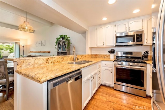 kitchen with appliances with stainless steel finishes, a sink, a peninsula, white cabinets, and light wood-style floors