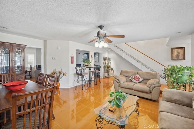 living room with ceiling fan, stairs, a textured ceiling, and light tile patterned floors
