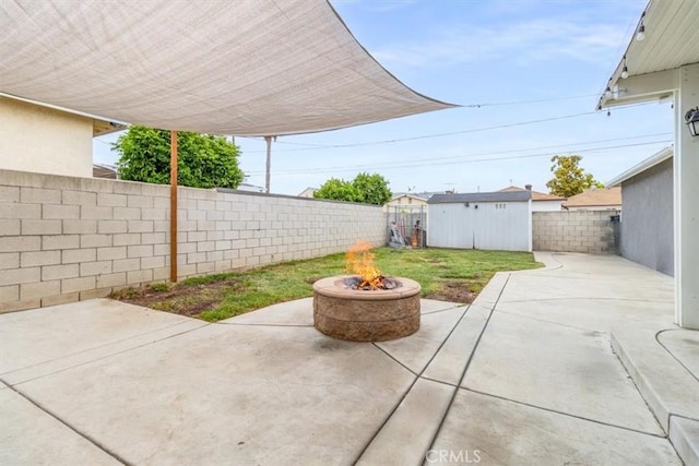 view of patio / terrace with an outdoor fire pit, a fenced backyard, a storage unit, and an outbuilding