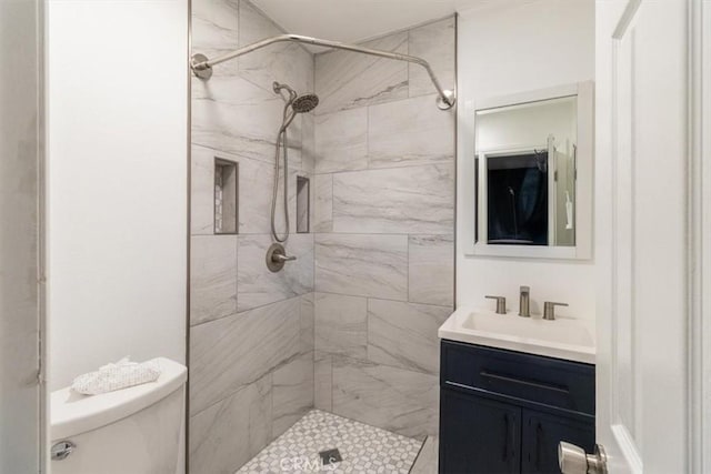 bathroom with a tile shower, vanity, and toilet