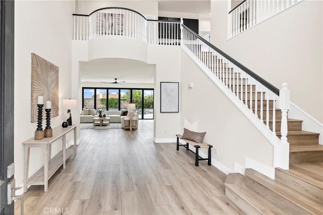 entryway featuring a high ceiling, stairs, wood finished floors, a ceiling fan, and baseboards