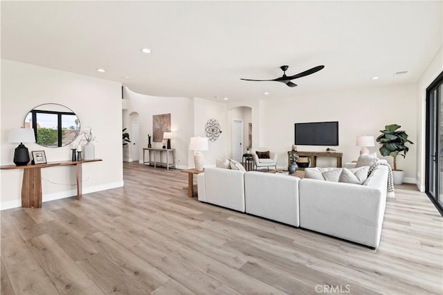 living area with arched walkways, ceiling fan, light wood finished floors, recessed lighting, and baseboards