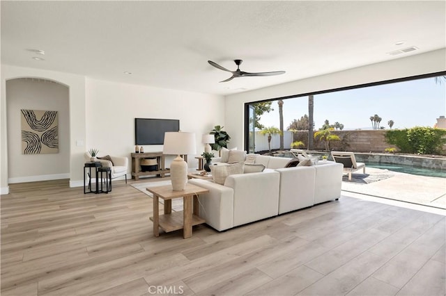 living area with a ceiling fan, light wood-style flooring, arched walkways, and baseboards