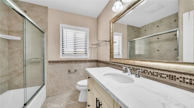 full bath featuring tile patterned flooring, tile walls, toilet, vanity, and combined bath / shower with glass door