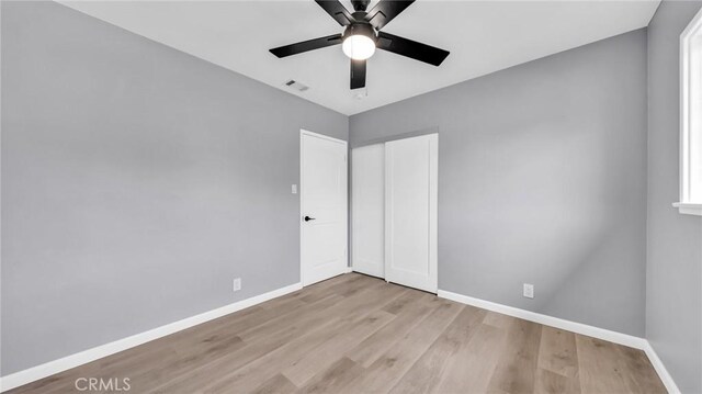 unfurnished bedroom with baseboards, wood finished floors, a closet, and a ceiling fan
