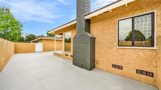 view of side of property with a patio, fence, a chimney, stucco siding, and crawl space