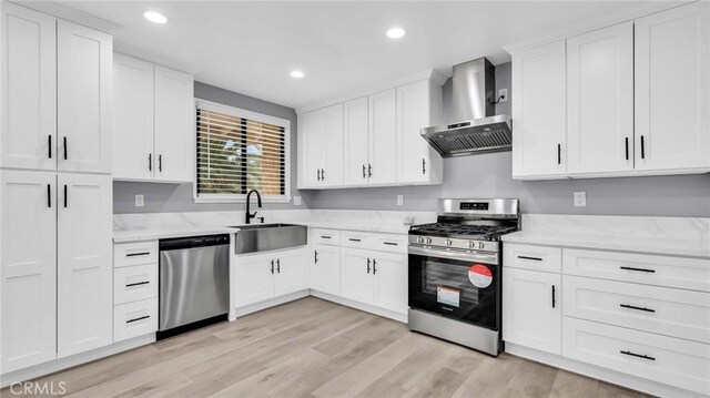 kitchen with appliances with stainless steel finishes, wall chimney range hood, a sink, recessed lighting, and white cabinets