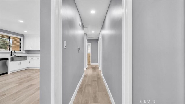 corridor featuring a sink, light wood-style flooring, recessed lighting, and baseboards