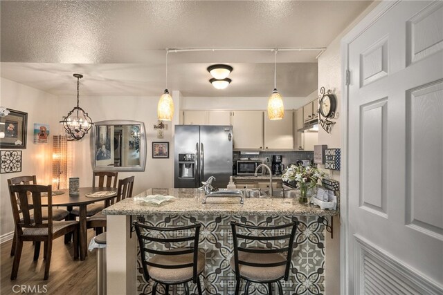 kitchen featuring stainless steel appliances, a peninsula, decorative backsplash, light stone countertops, and dark wood-type flooring