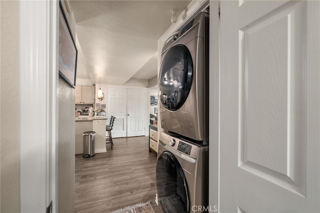 laundry room with stacked washing machine and dryer, wood finished floors, and a textured ceiling