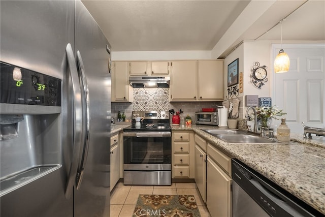kitchen with appliances with stainless steel finishes, under cabinet range hood, cream cabinets, a sink, and light tile patterned floors