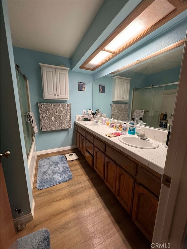 7477 Corona Ave, Hesperia, CA 92345 - full bathroom featuring double vanity, wood finished floors, enclosed tub / shower combo, and baseboards