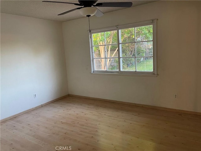 spare room with light wood-type flooring, a ceiling fan, baseboards, and a textured ceiling