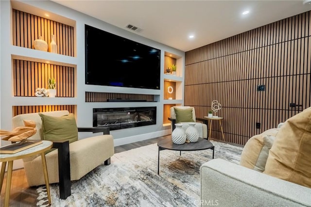 living area featuring wood finished floors, a glass covered fireplace, recessed lighting, and built in features