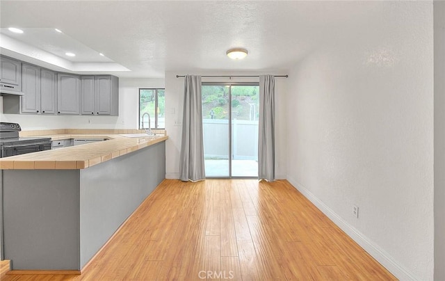 1207 Porto Grande Unit 1, Diamond Bar, CA 91765 - kitchen with black range with electric cooktop, baseboards, gray cabinets, tile counters, and light wood-type flooring