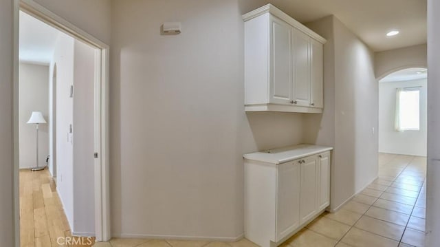 corridor featuring arched walkways, recessed lighting, baseboards, and light tile patterned floors