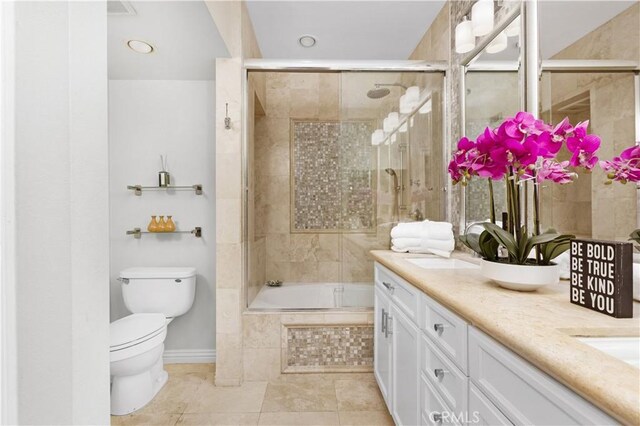 bathroom featuring toilet, double vanity, tile patterned flooring, baseboards, and tiled shower / bath