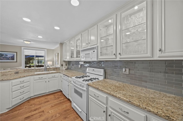 kitchen featuring white appliances, a sink, light wood-style flooring, white cabinetry, and glass insert cabinets