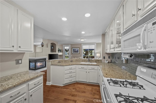 kitchen featuring white appliances, dark wood-type flooring, white cabinets, a peninsula, and a sink
