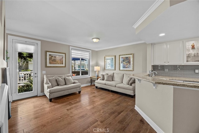 living area with healthy amount of natural light, ornamental molding, wood finished floors, and baseboards