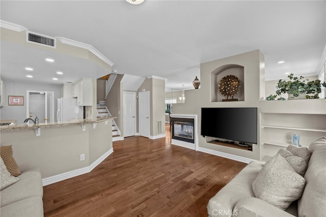living area with crown molding, dark wood finished floors, a glass covered fireplace, baseboards, and stairs