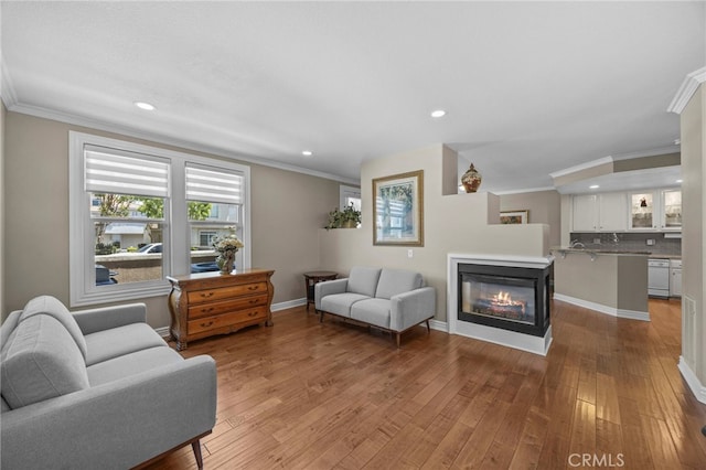 living room with a glass covered fireplace, ornamental molding, recessed lighting, light wood-type flooring, and baseboards
