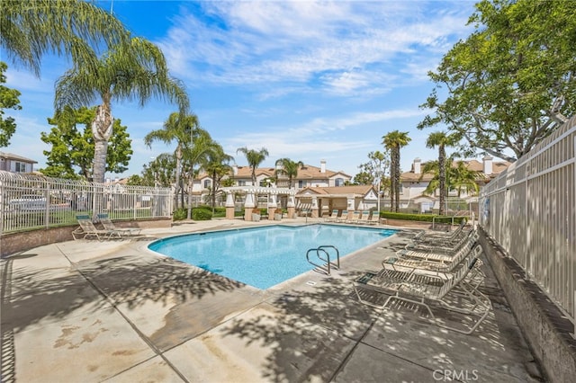 community pool featuring fence, a patio, and a residential view