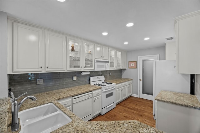 kitchen featuring white appliances, a sink, wood finished floors, white cabinetry, and recessed lighting